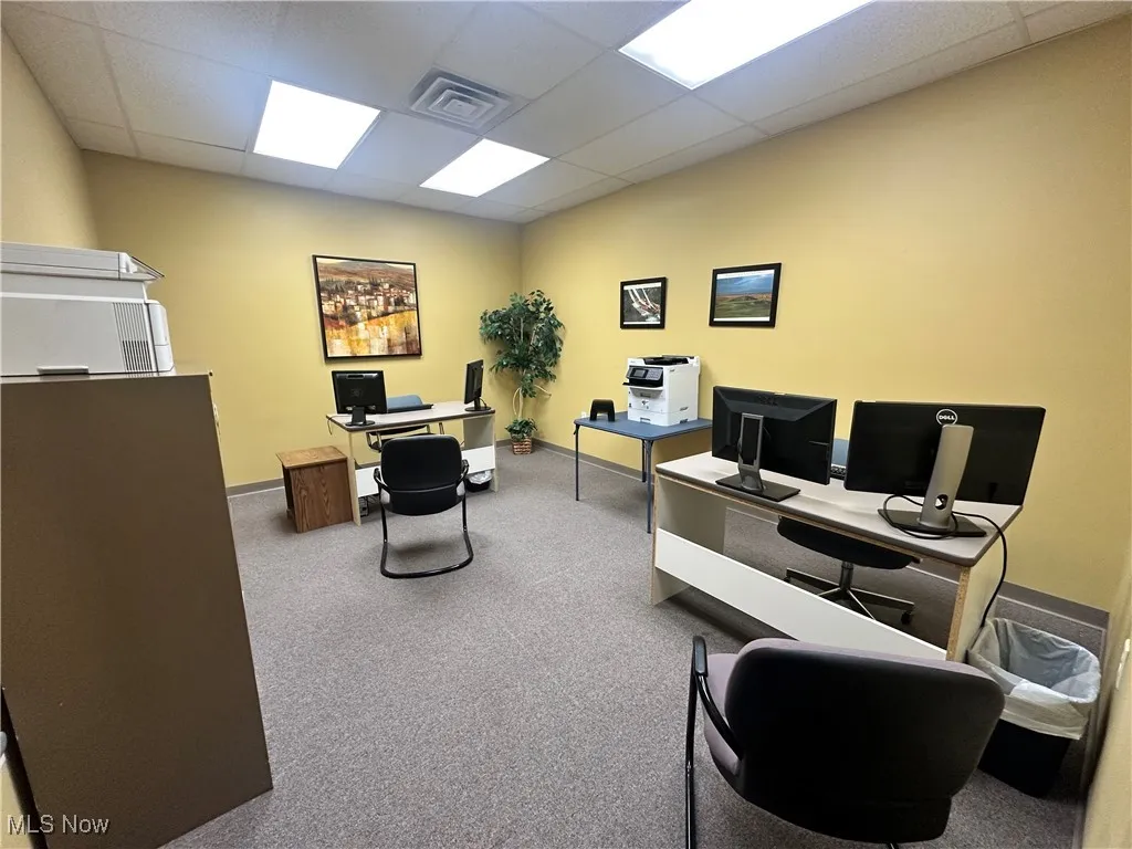 Carpeted office space with a drop ceiling and baseboards