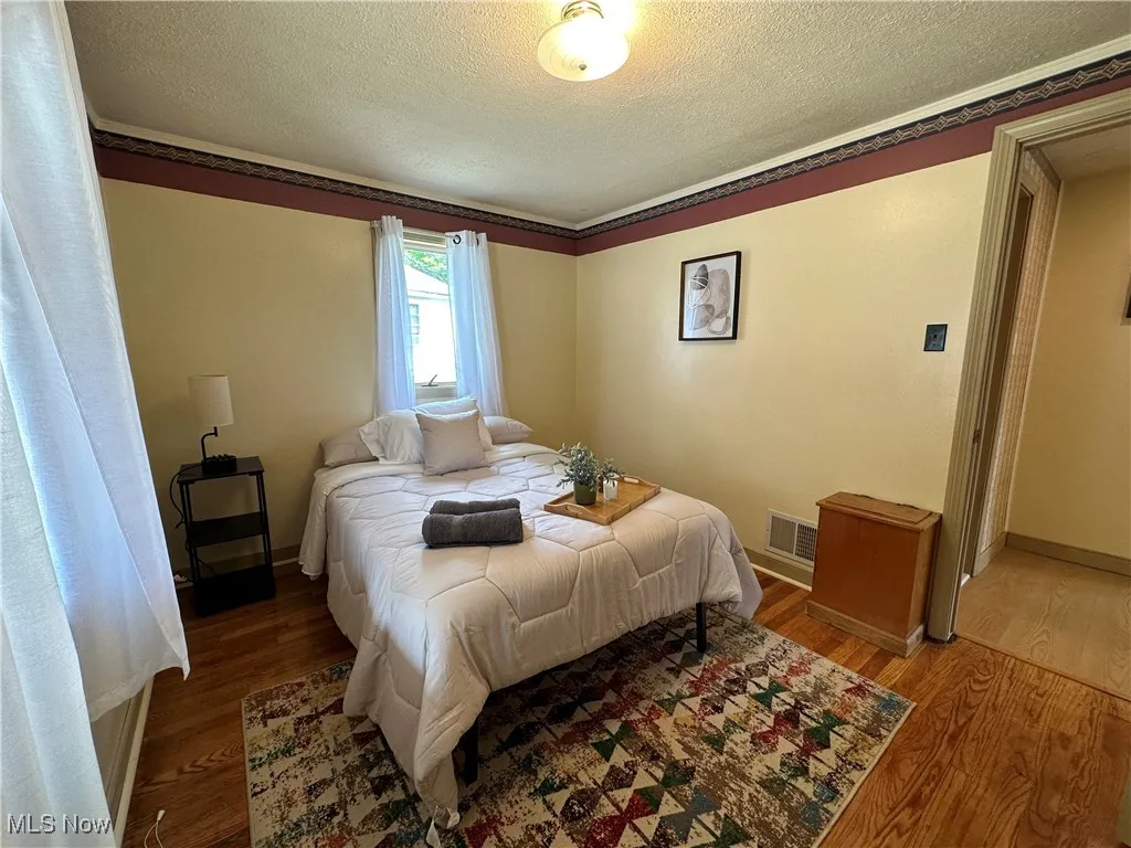 Bedroom featuring a textured ceiling, wood finished floors, visible vents, and baseboards