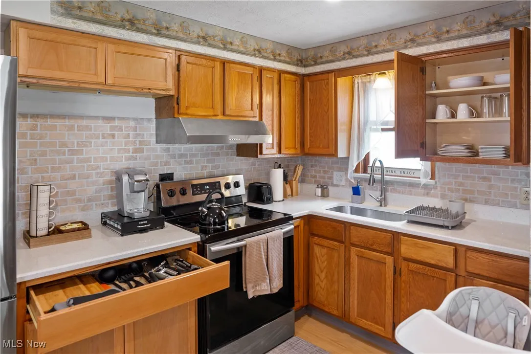 Kitchen with under cabinet range hood, a sink, light countertops, brown cabinets, and stainless steel electric range oven