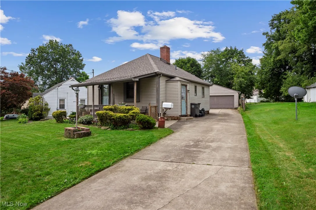 View of side of home with a garage, an outdoor structure, a yard, roof with shingles, and a chimney