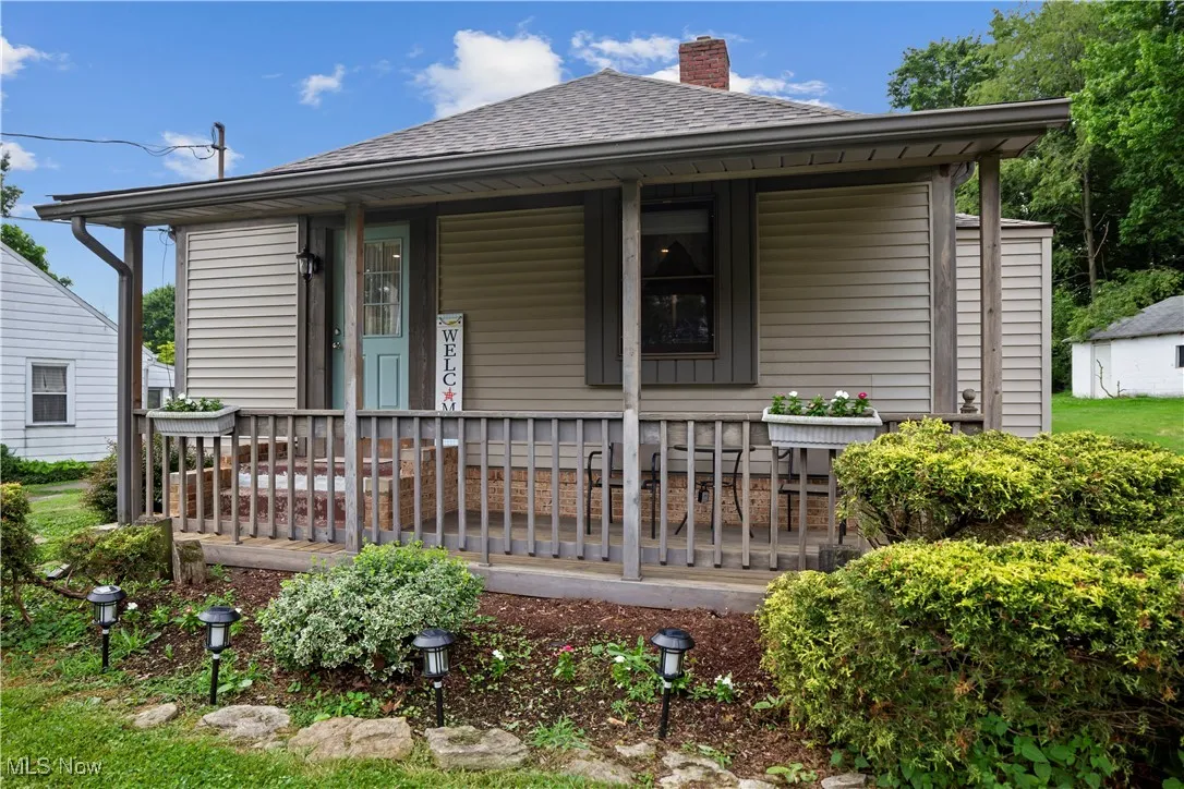 View of front of home with a shingled roof, a chimney, and a porch