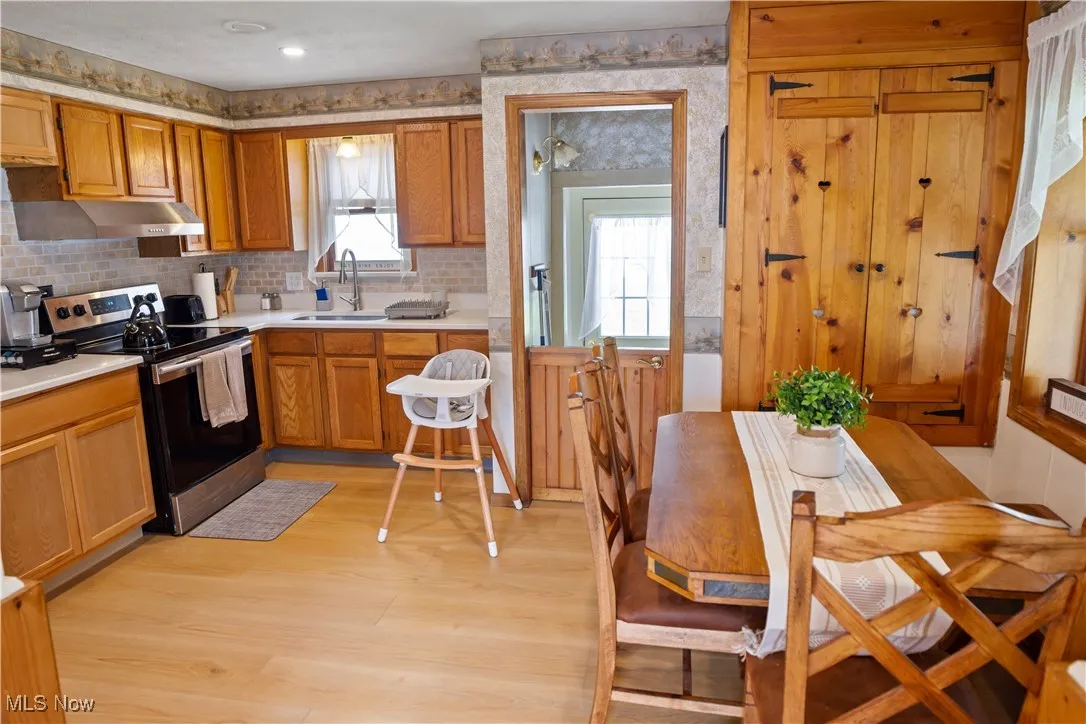 Kitchen featuring light countertops, light wood-style floors, a sink, under cabinet range hood, and stainless steel electric range