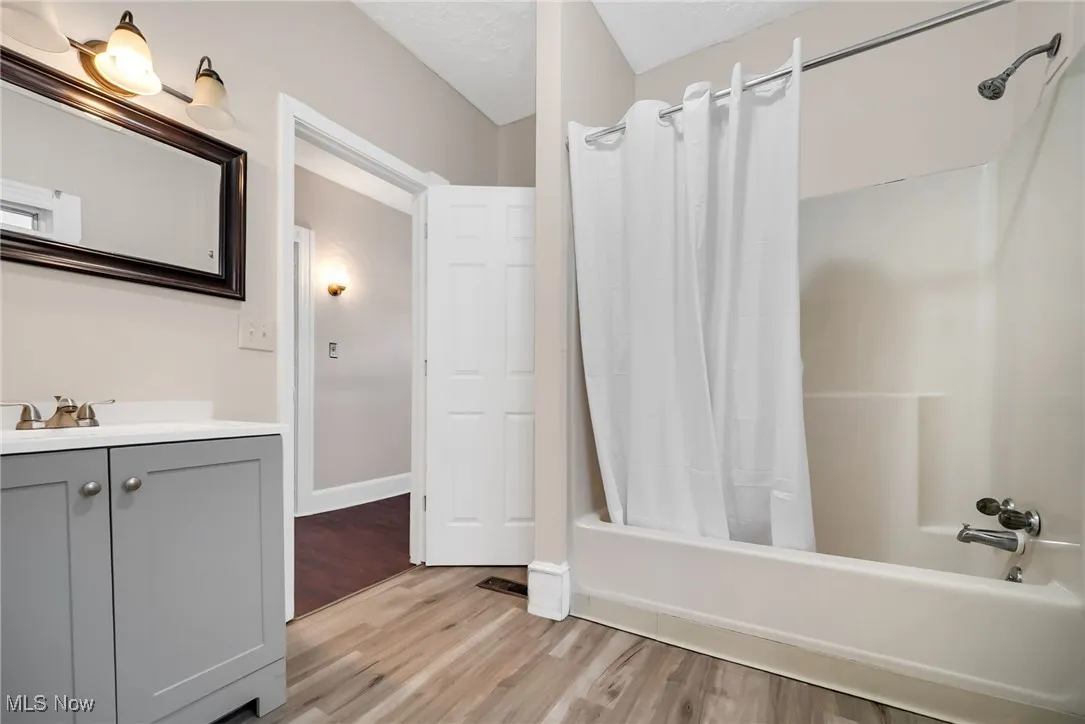 Bathroom featuring shower / bath combo, wood finished floors, vanity, and baseboards