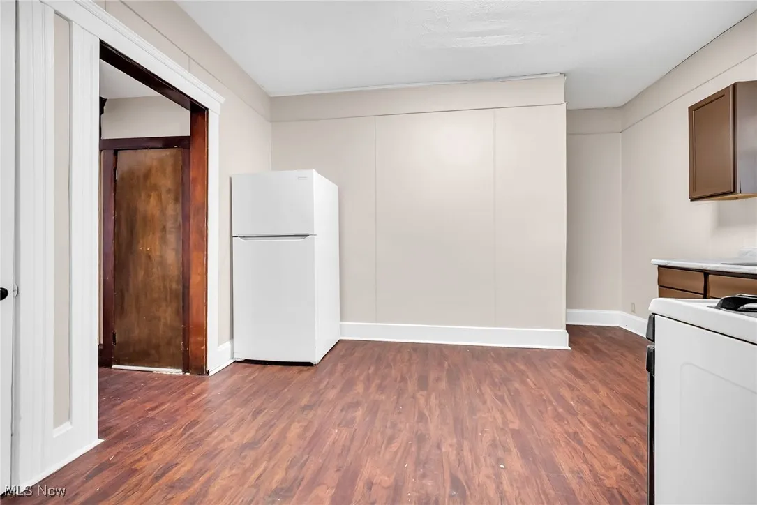 Kitchen with freestanding refrigerator, dark wood-style flooring, range, and baseboards