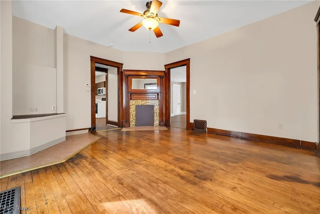 Unfurnished living room with visible vents, a fireplace with flush hearth, ceiling fan, baseboards, and hardwood / wood-style flooring