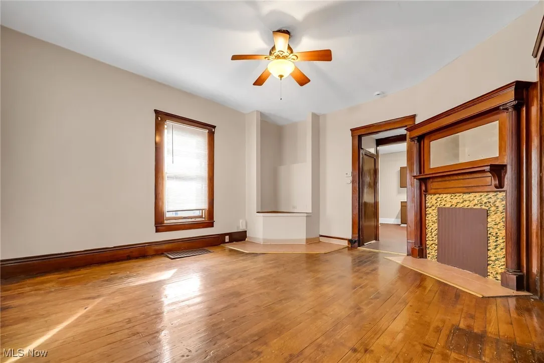 Unfurnished living room featuring wood-type flooring, a tile fireplace, a ceiling fan, and baseboards