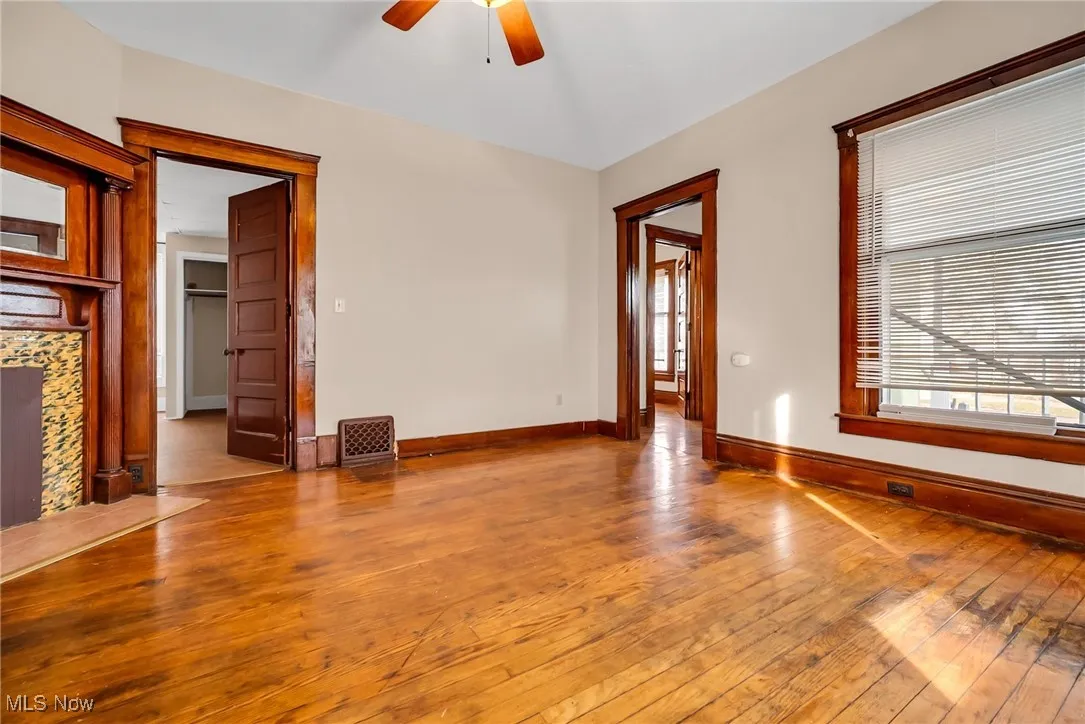 Unfurnished living room featuring wood-type flooring, a tiled fireplace, baseboards, and a ceiling fan