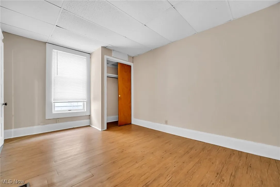 Empty room with light wood-style floors, a drop ceiling, and baseboards