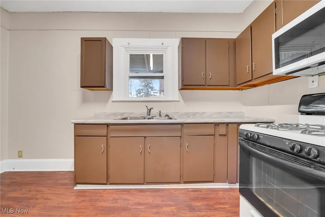 Kitchen featuring baseboards, wood finished floors, light countertops, a sink, and gas stove