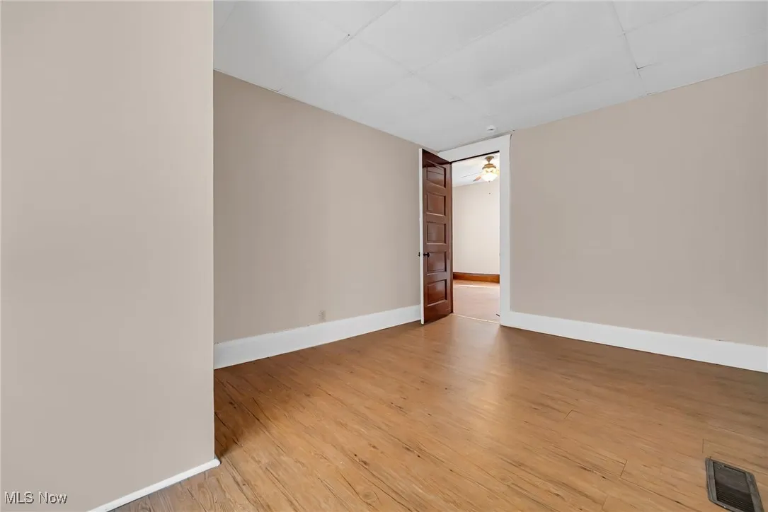 Empty room featuring visible vents, light wood-style floors, a ceiling fan, a drop ceiling, and baseboards