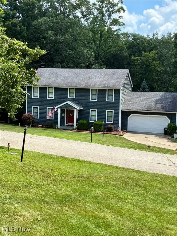 Colonial-style house with an attached garage, a front lawn, driveway, and a shingled roof