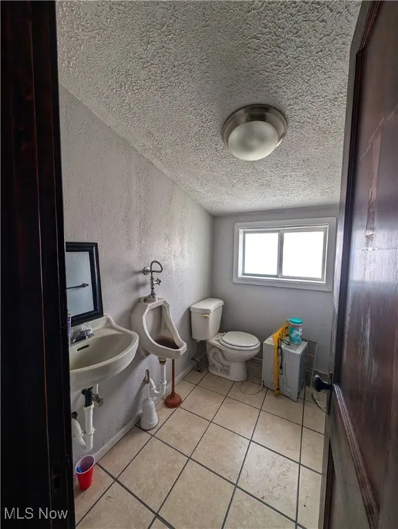 Bathroom with a textured ceiling, a textured wall, toilet, baseboards, and tile patterned floors