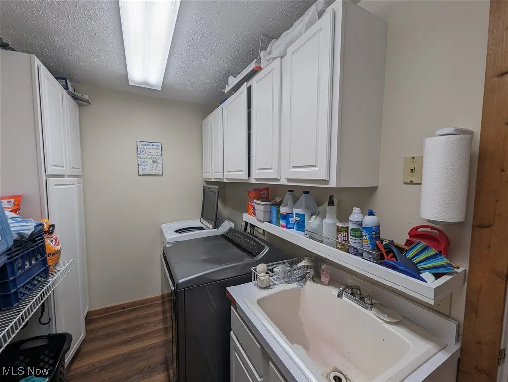 Washroom featuring washing machine and clothes dryer, cabinet space, dark wood finished floors, and a textured ceiling