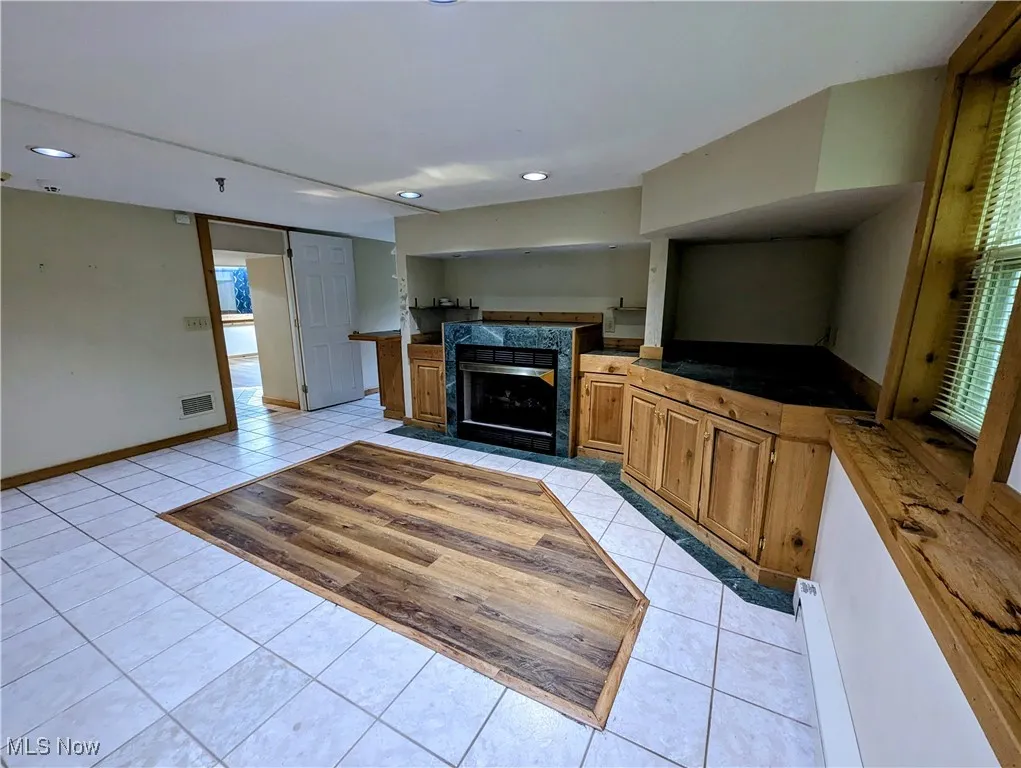 Unfurnished living room featuring light tile patterned flooring, a tiled fireplace, recessed lighting, and baseboards