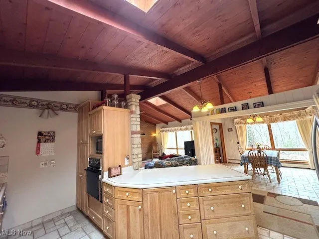 Kitchen featuring stone tile flooring, light countertops, hanging light fixtures, lofted ceiling with beams, and black oven