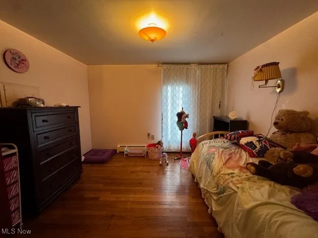 Bedroom with a baseboard heating unit and dark wood-type flooring