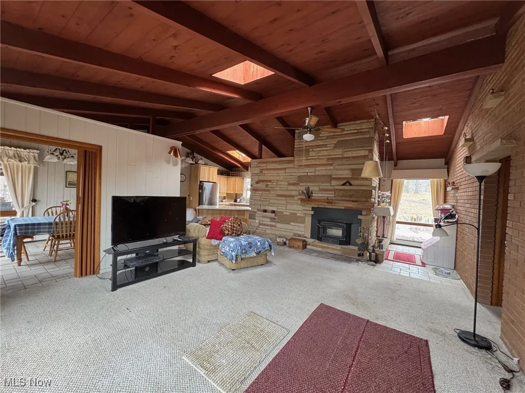 Living room with wooden ceiling, vaulted ceiling with skylight, ceiling fan, and light colored carpet