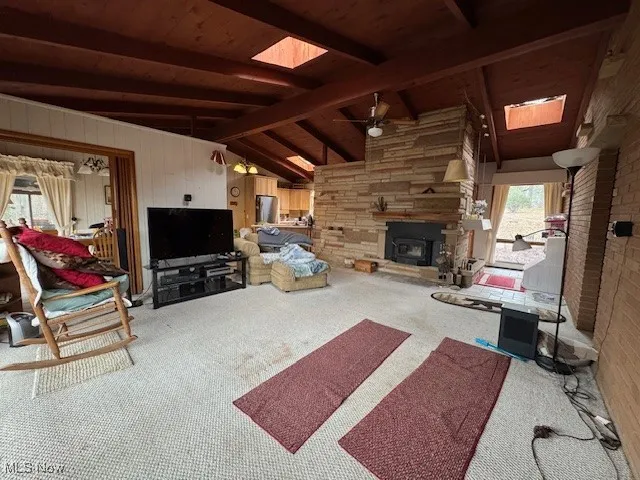 Carpeted living area featuring a ceiling fan, lofted ceiling with skylight, wood ceiling, and wooden walls