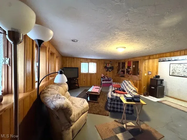 Living room with concrete flooring, wood walls, and a textured ceiling
