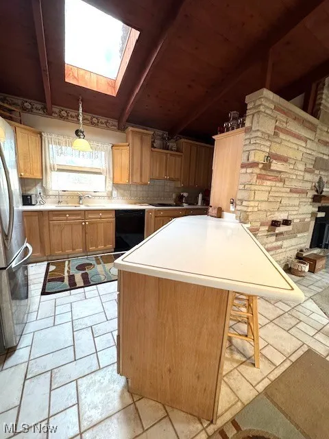 Kitchen with black dishwasher, light countertops, decorative backsplash, freestanding refrigerator, and a sink