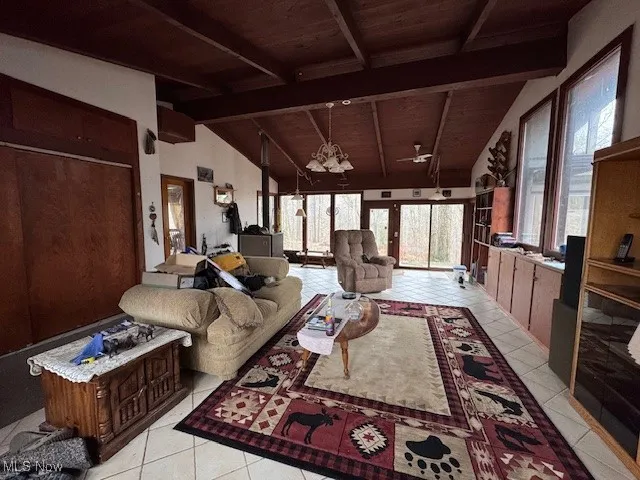 Living room featuring light tile patterned floors, wooden ceiling, vaulted ceiling with beams, a wood stove, and a chandelier