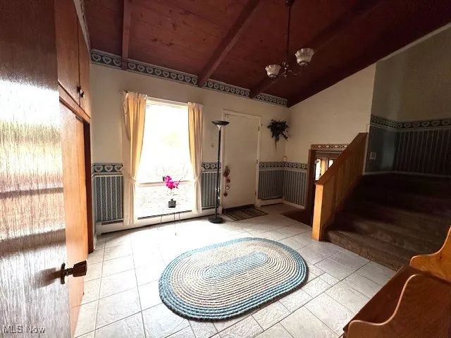 Entryway with vaulted ceiling with beams, light tile patterned floors, an inviting chandelier, wooden ceiling, and stairs
