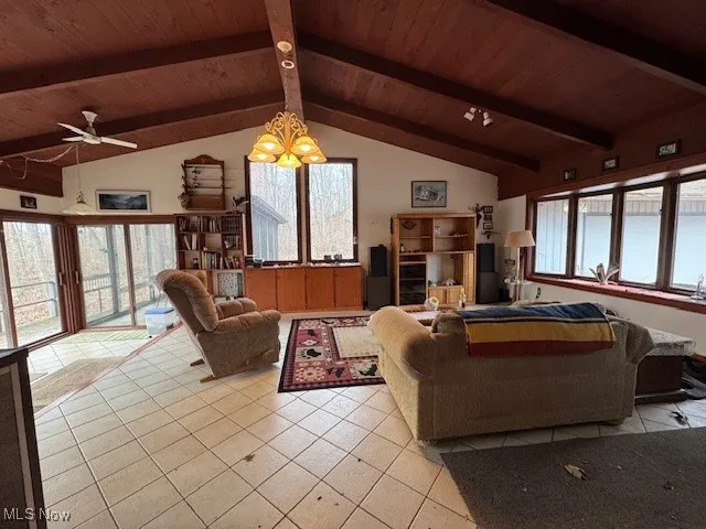 Living area with lofted ceiling with beams, light tile patterned floors, wooden ceiling, and a chandelier
