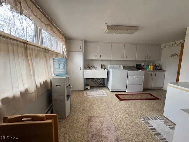 Clothes washing area featuring cabinet space, light floors, a sink, and washing machine and clothes dryer