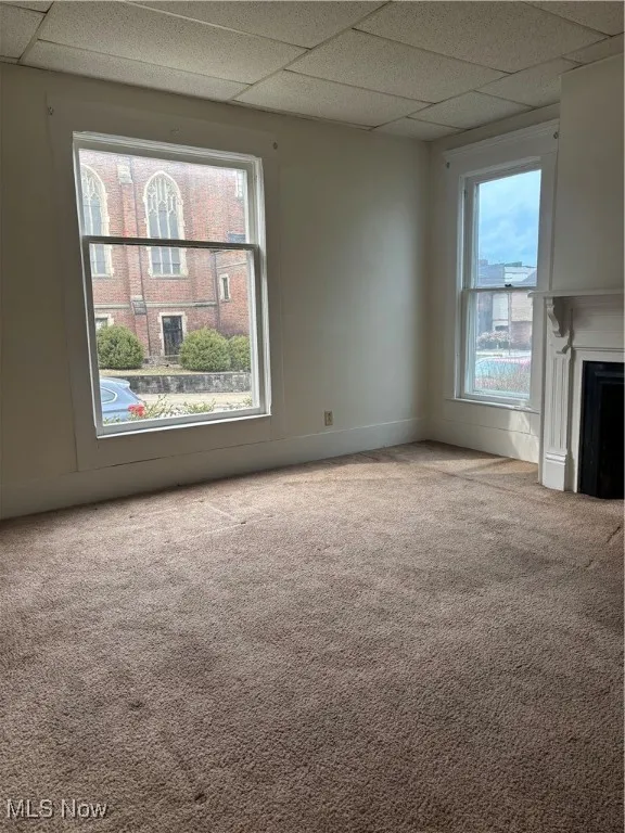 Unfurnished living room featuring a paneled ceiling, carpet flooring, and a fireplace