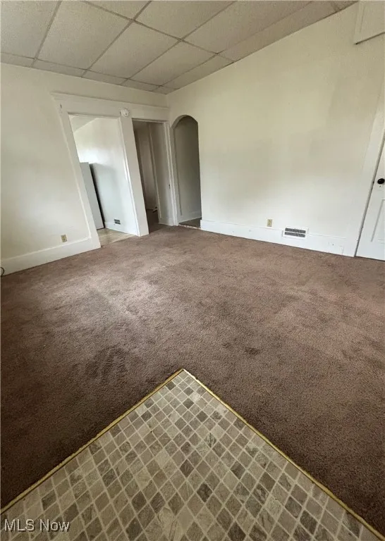 Spare room featuring visible vents, arched walkways, baseboards, carpet, and a paneled ceiling