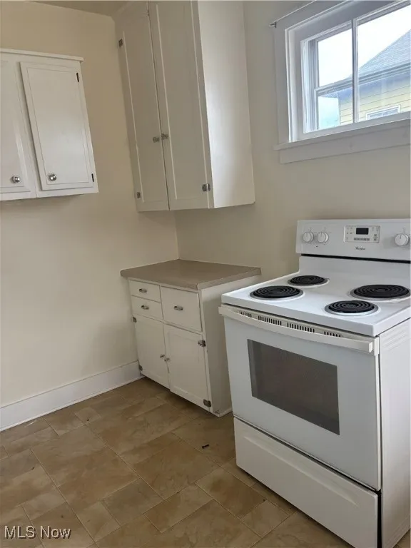 Kitchen with baseboards, light countertops, stove, and white cabinets