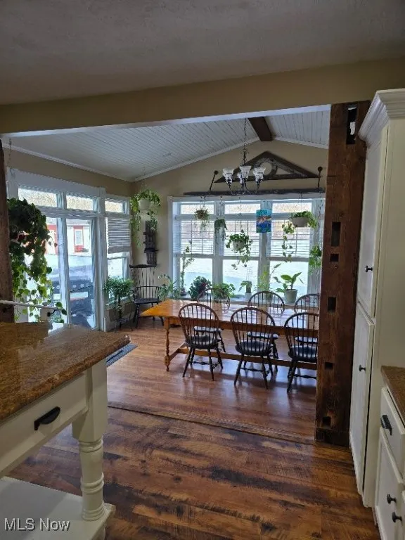Dining space with vaulted ceiling with beams, ornate columns, a chandelier, and dark wood-style flooring