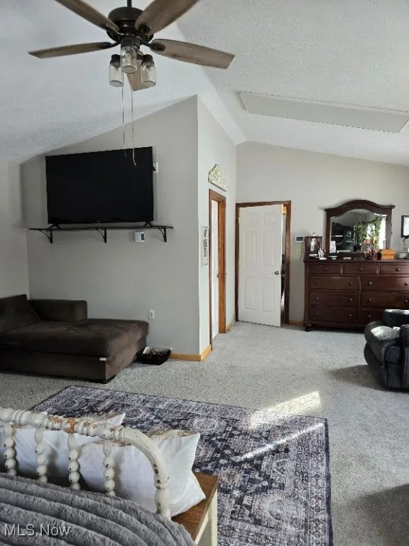 Carpeted living area featuring vaulted ceiling, a textured ceiling, a ceiling fan, and baseboards