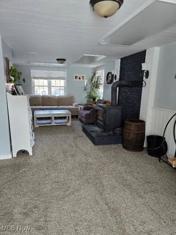 Carpeted living area featuring wainscoting, plenty of natural light, and a wood stove