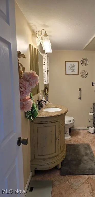 Half bathroom with toilet, baseboards, and vanity