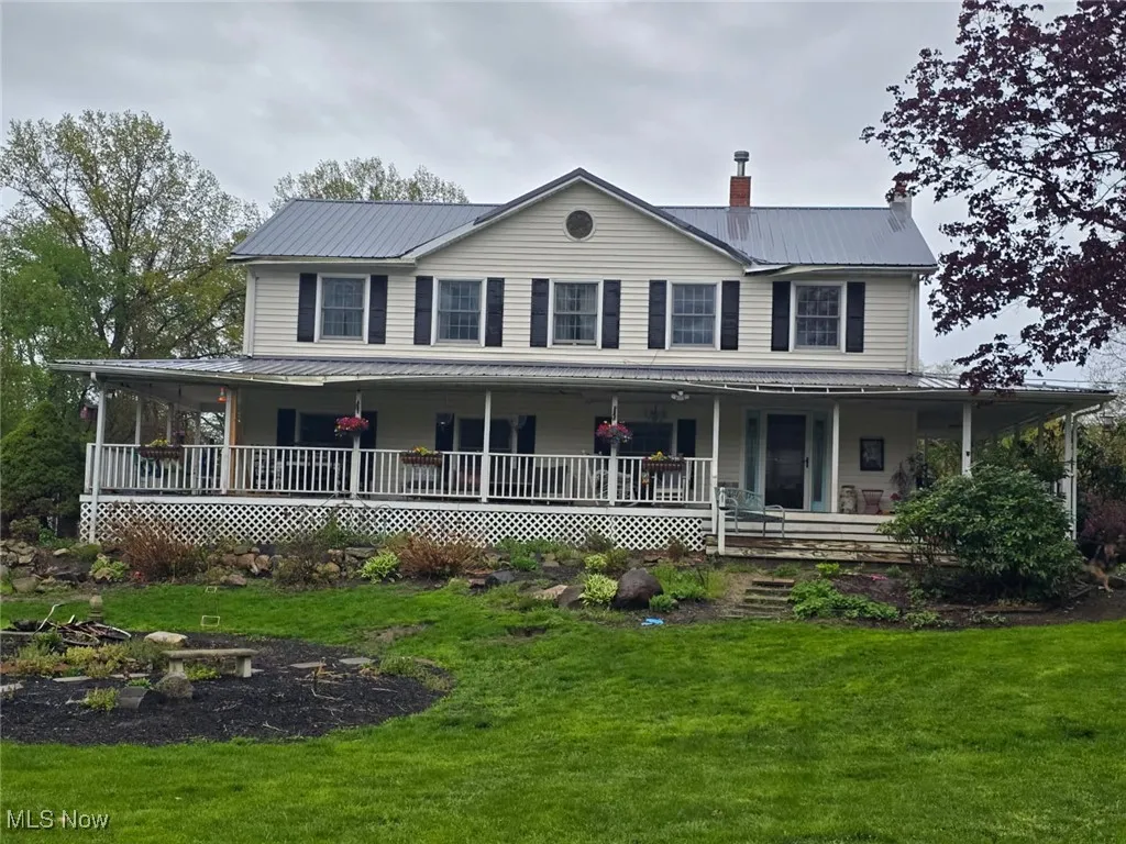 Farmhouse featuring a porch, a chimney, metal roof, and a front lawn