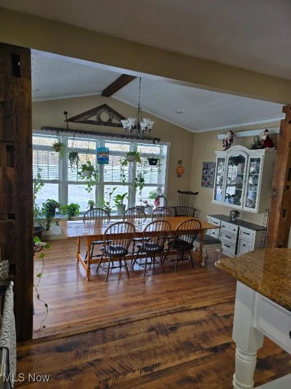 Dining room with dark wood-type flooring, a notable chandelier, and lofted ceiling with beams
