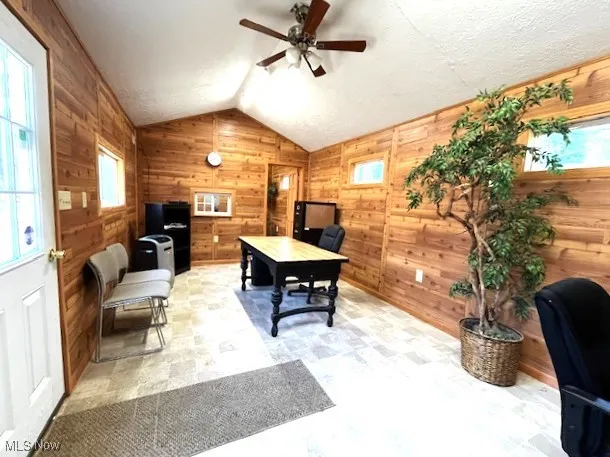 Office featuring vaulted ceiling, knotty pine walls, a ceiling fan, and a healthy amount of sunlight