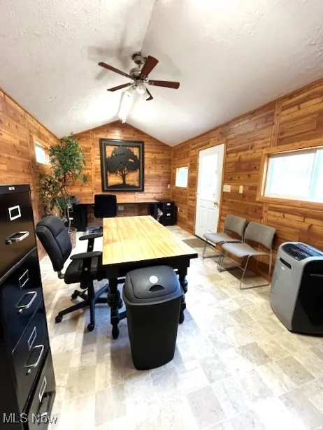 Office with lofted ceiling, wood walls, ceiling fan, and a textured ceiling