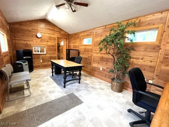 Office area featuring lofted ceiling, wood walls, a ceiling fan.