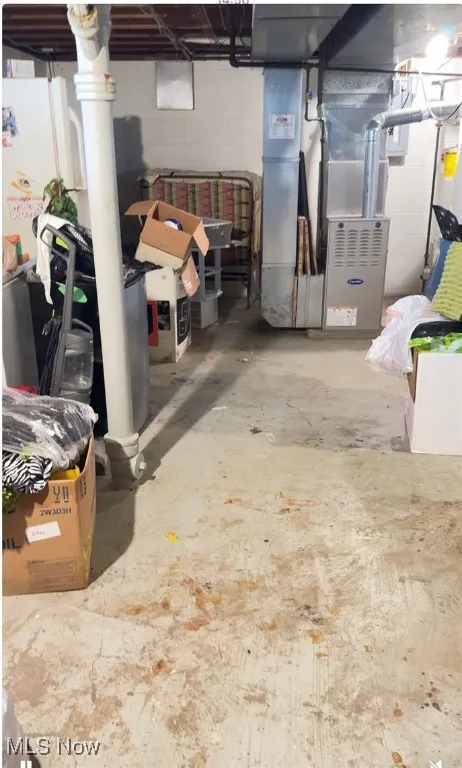 Unfinished below grade area with heating unit, water heater, and freestanding refrigerator
