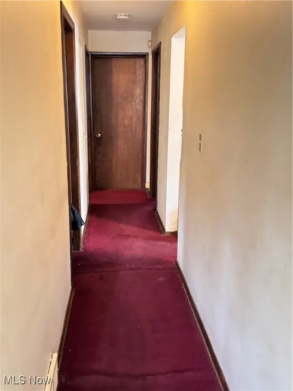 Hallway featuring dark carpet and baseboards