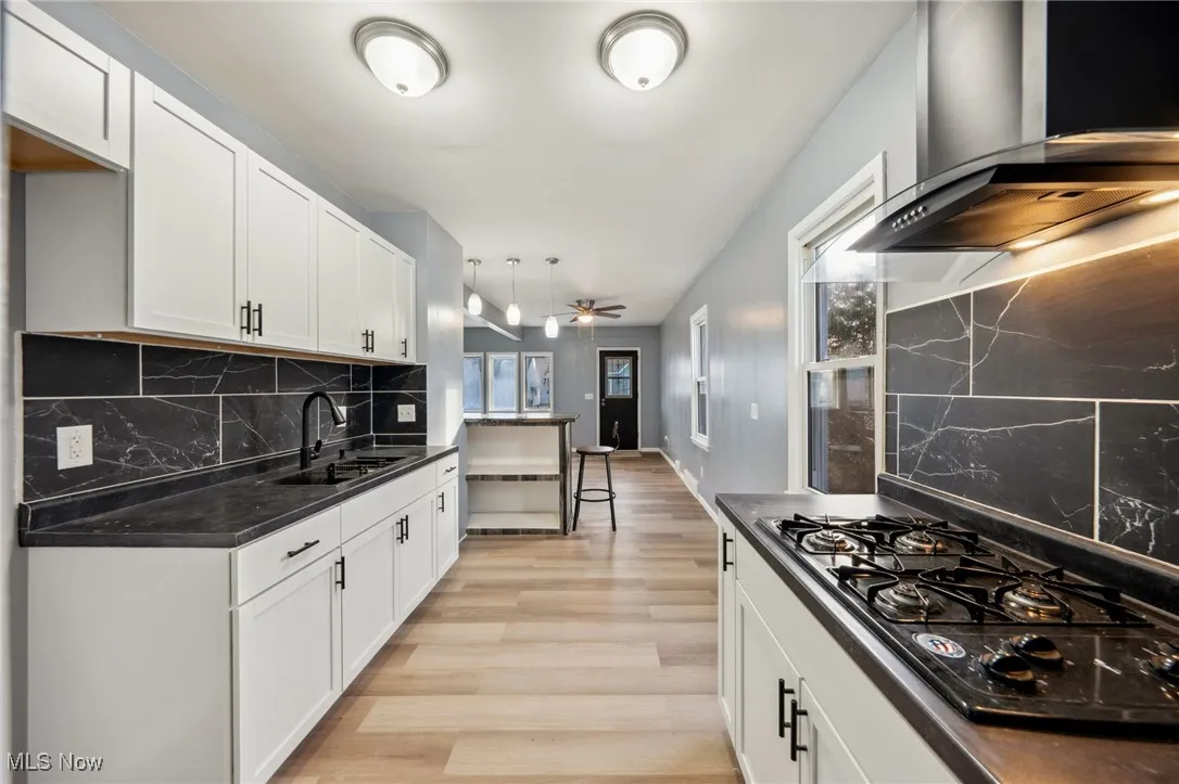 Kitchen with black gas cooktop, dark countertops, light wood-style floors, a sink, and wall chimney exhaust hood