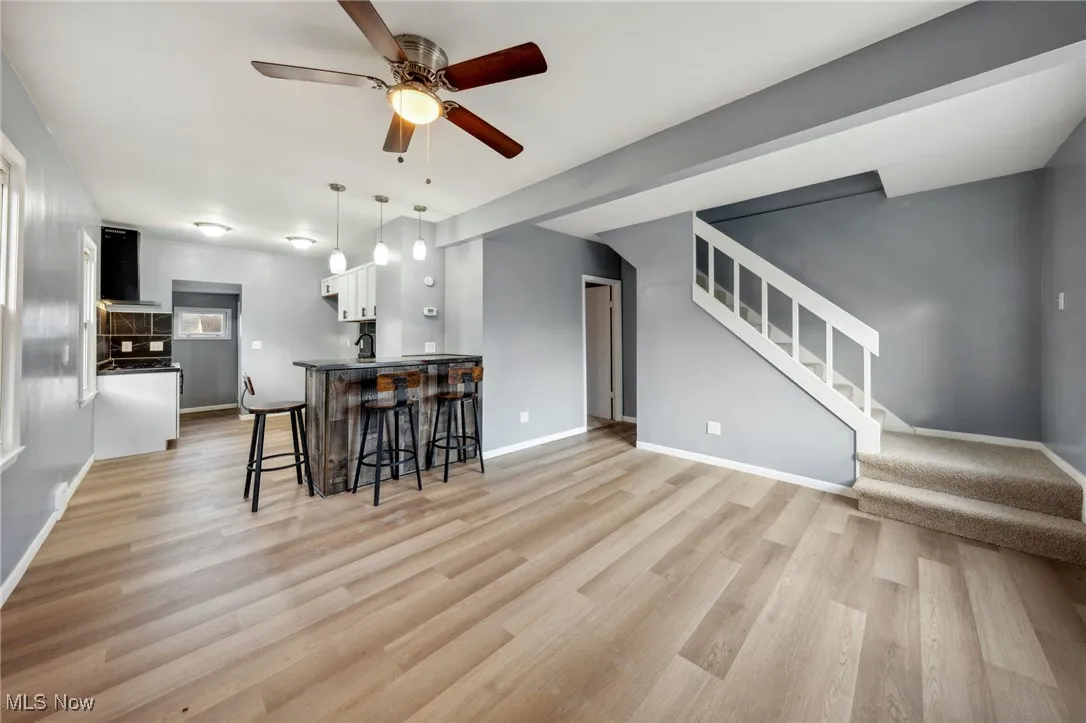 Kitchen with light wood finished floors, baseboards, a kitchen breakfast bar, ventilation hood, and white cabinetry