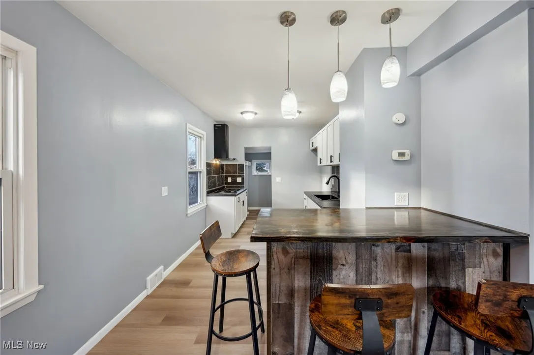 Kitchen with dark countertops, a peninsula, light wood-type flooring, a sink, and exhaust hood