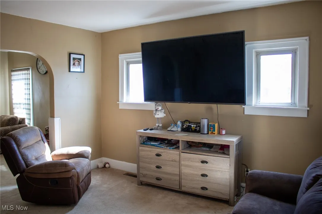 Living area with baseboards, arched walkways, a wealth of natural light, and light colored carpet
