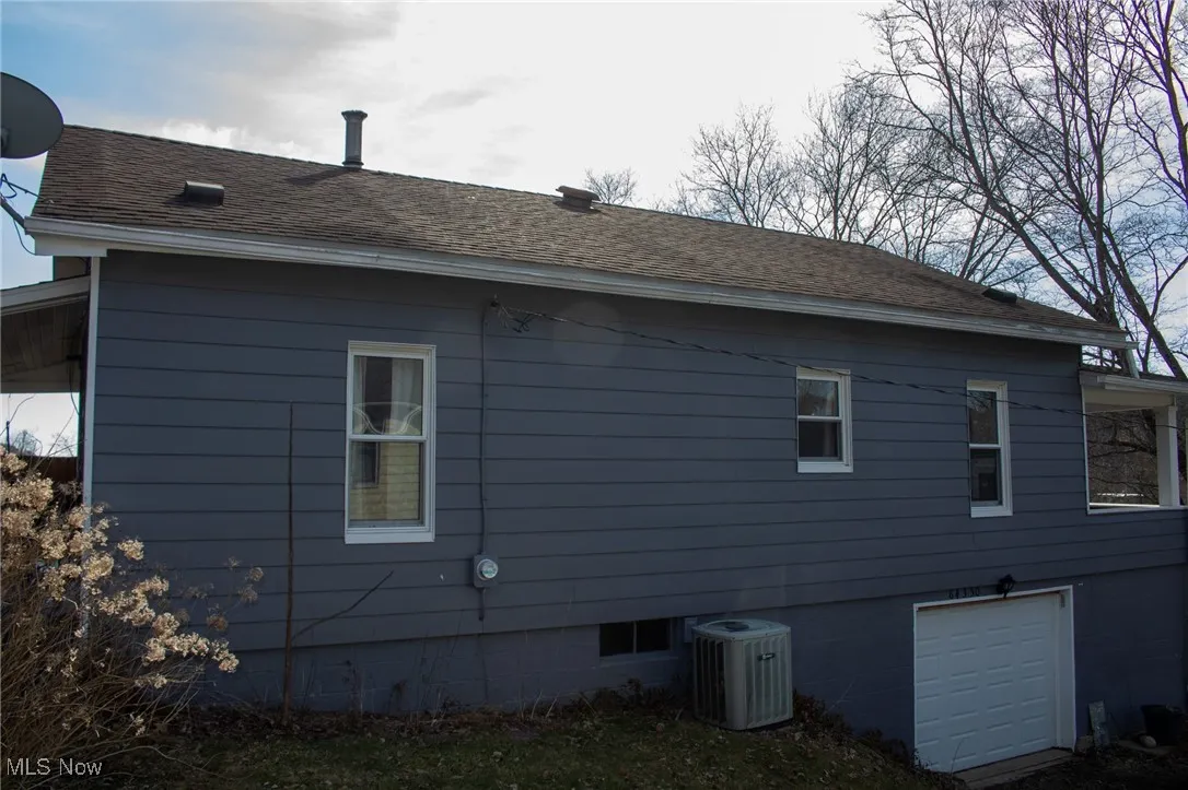 View of home's exterior featuring cooling unit, roof with shingles, and an attached garage