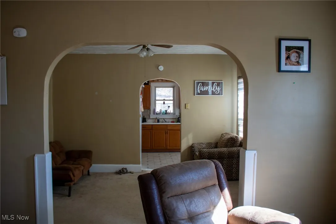 Sitting room with arched walkways, ceiling fan, baseboards, and light colored carpet
