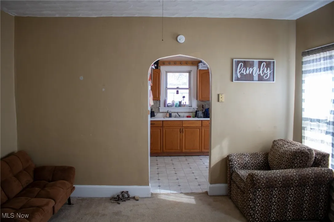 Living area with baseboards, arched walkways, and light colored carpet
