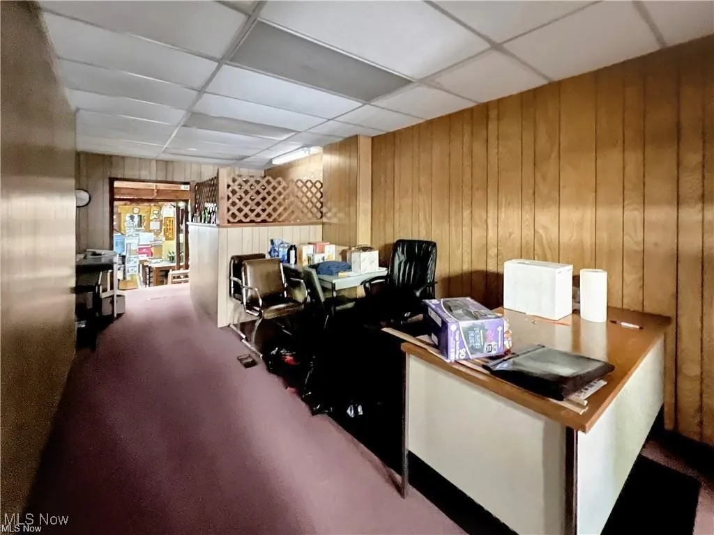 Office area featuring a drop ceiling and wood walls